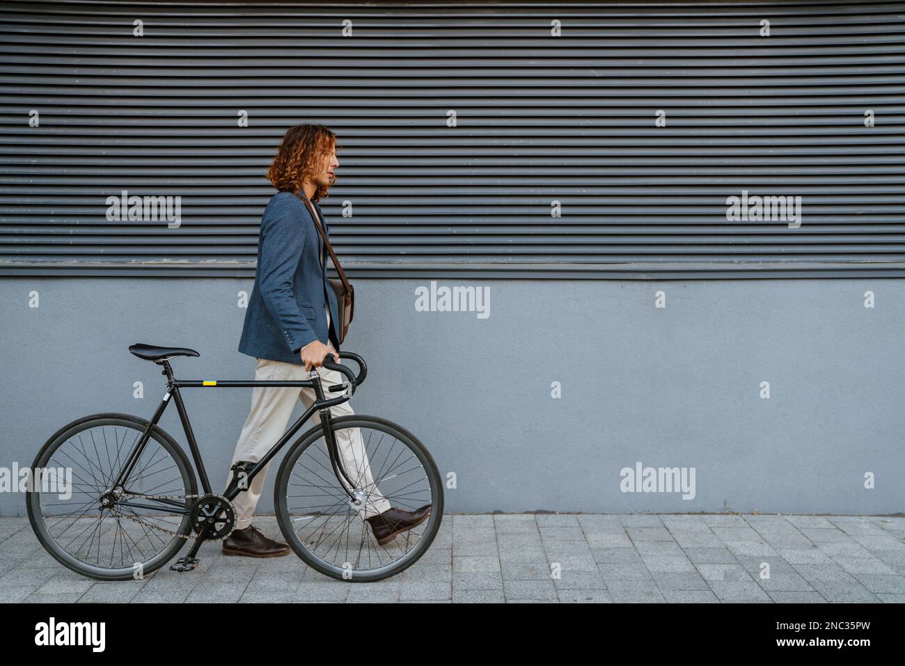 Ginger homme européen marchant avec un vélo près du mur gris en plein air sur la rue de la ville Banque D'Images