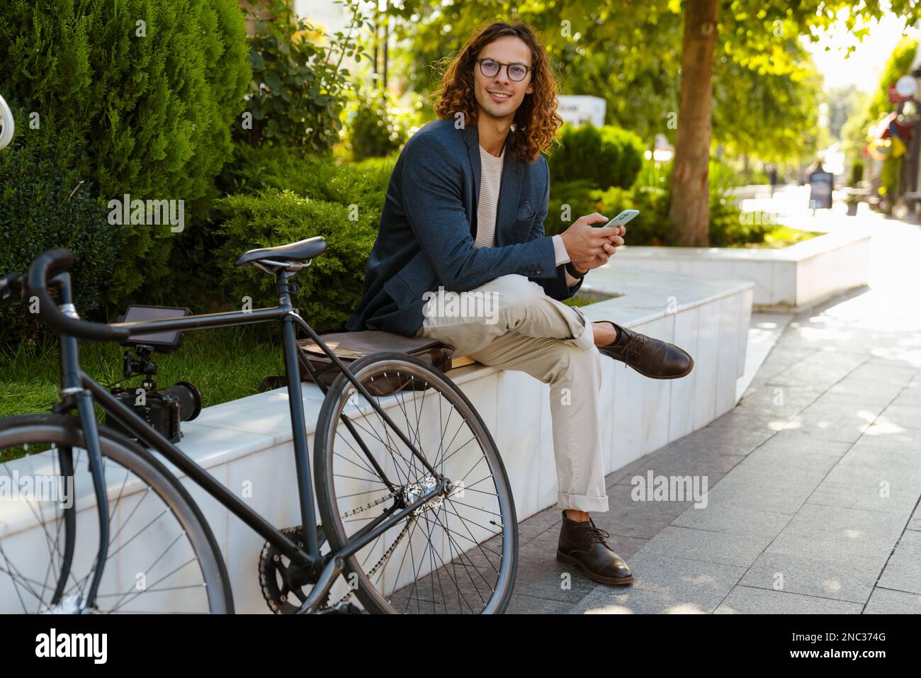 Ginger homme européen utilisant un téléphone portable tout en étant assis avec un vélo dans le parc de la ville Banque D'Images