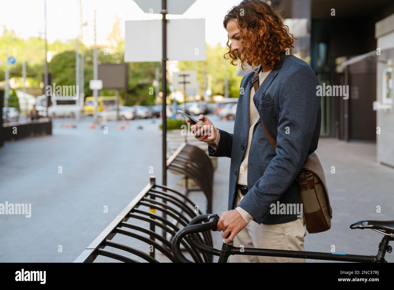 Ginger homme européen utilisant le téléphone portable tout en étant debout avec un vélo sur la rue de la ville Banque D'Images