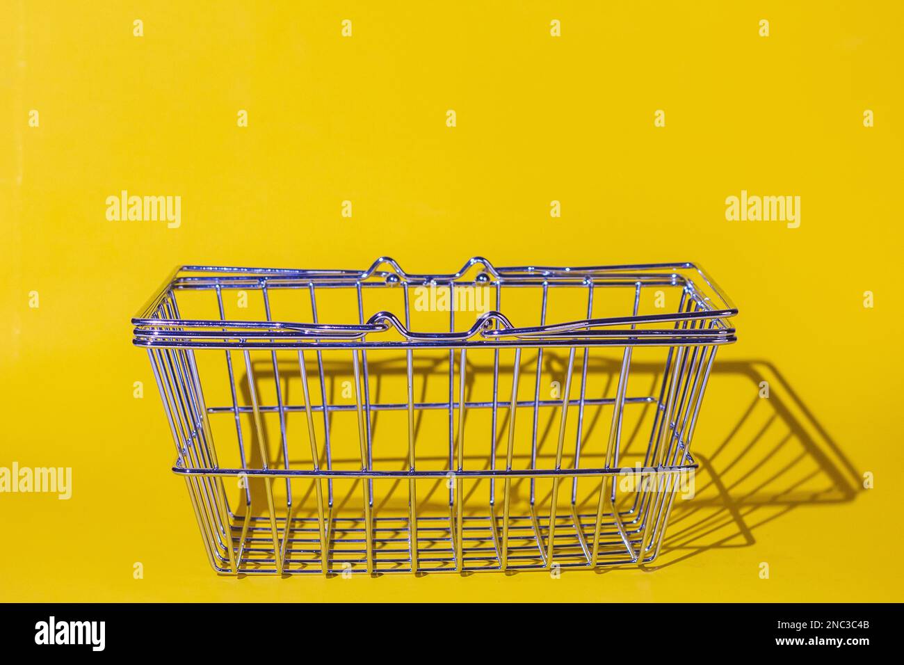 panier vide dans le supermarché isolé, objet unique, grille métallique chromée, supports sur la surface du fond jaune.conce Banque D'Images