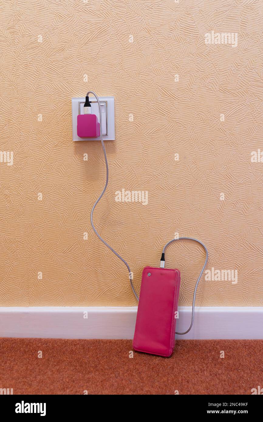 Téléphone portable sur un sol avec étui rose branché et recharge avec une fiche USB rose et un câble. Concept: Femmes et technologie, accessoire de téléphone féminin Banque D'Images