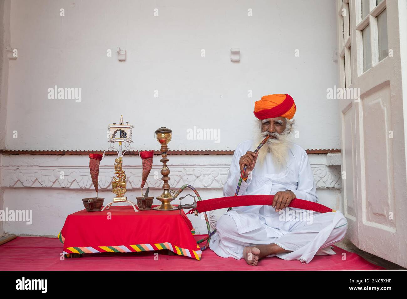 Jodhpur, Rajasthan, Inde - 19 octobre 2019 : Rajput homme âgé fumant à travers un narguilé, portant Marathi pagri et épée sur les genoux. Banque D'Images