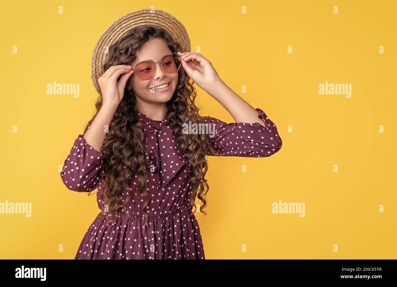 enfant positif en chapeau de paille et lunettes de soleil avec de longs cheveux bruns sur fond jaune Banque D'Images