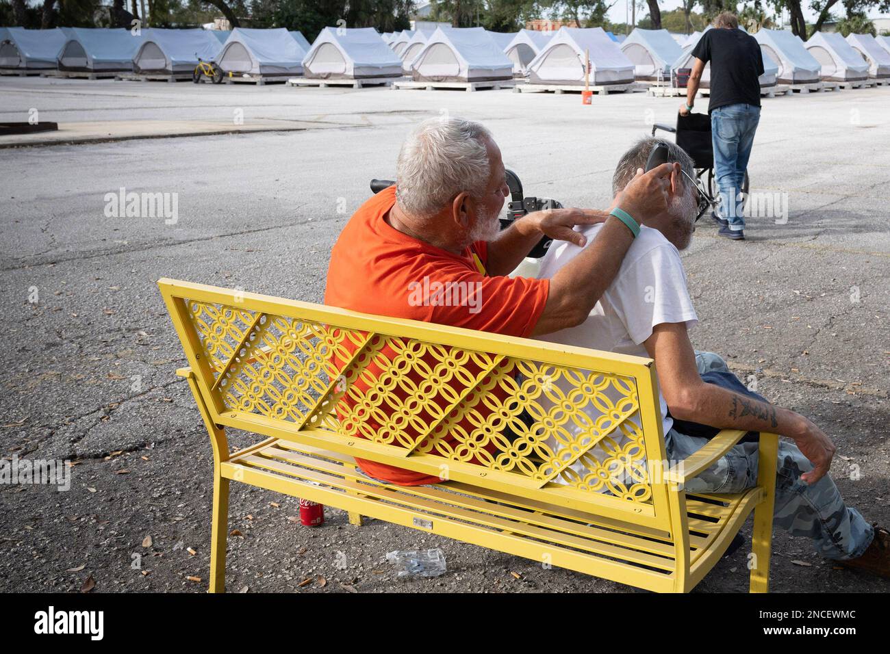 Tampa, Floride, États-Unis. 30th décembre 2022. Assis sur un banc à l'extérieur et près des rangées de tentes, RICARDO GARCIA, 70, connu sous le nom de ‚'Limo‚' à ses amis, utilise des tondeuses pour donner à un autre résident une coupe de cheveux au Tampa Hope Shelter. (Credit image: © Robin Rayne/ZUMA Press Wire) USAGE ÉDITORIAL SEULEMENT! Non destiné À un usage commercial ! Banque D'Images