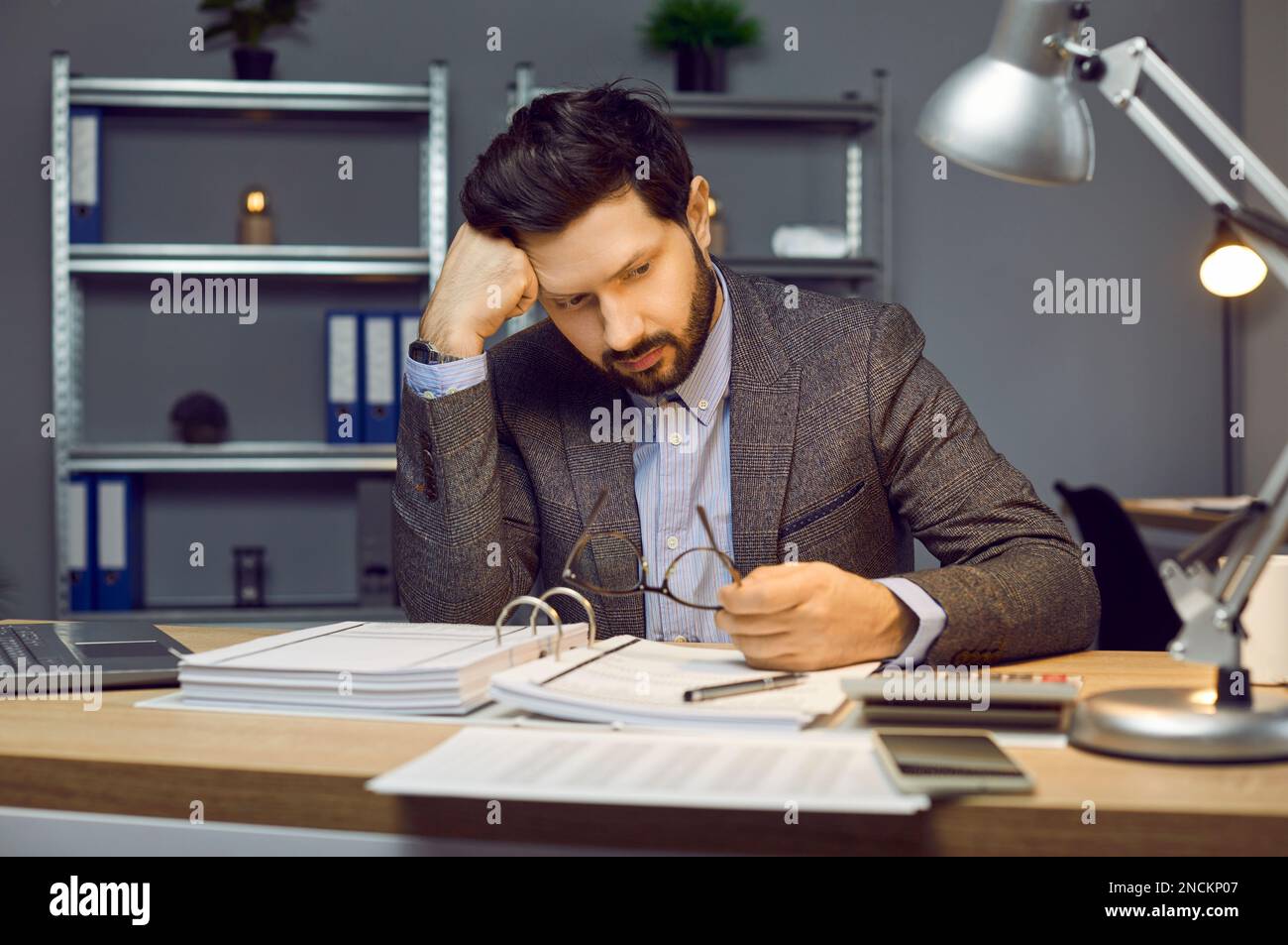 Portrait de frustré, réfléchi, barbu jeune homme de comptable ou d'entrepreneur assis dans le bureau à son lieu de travail avec un grand dossier de Banque D'Images