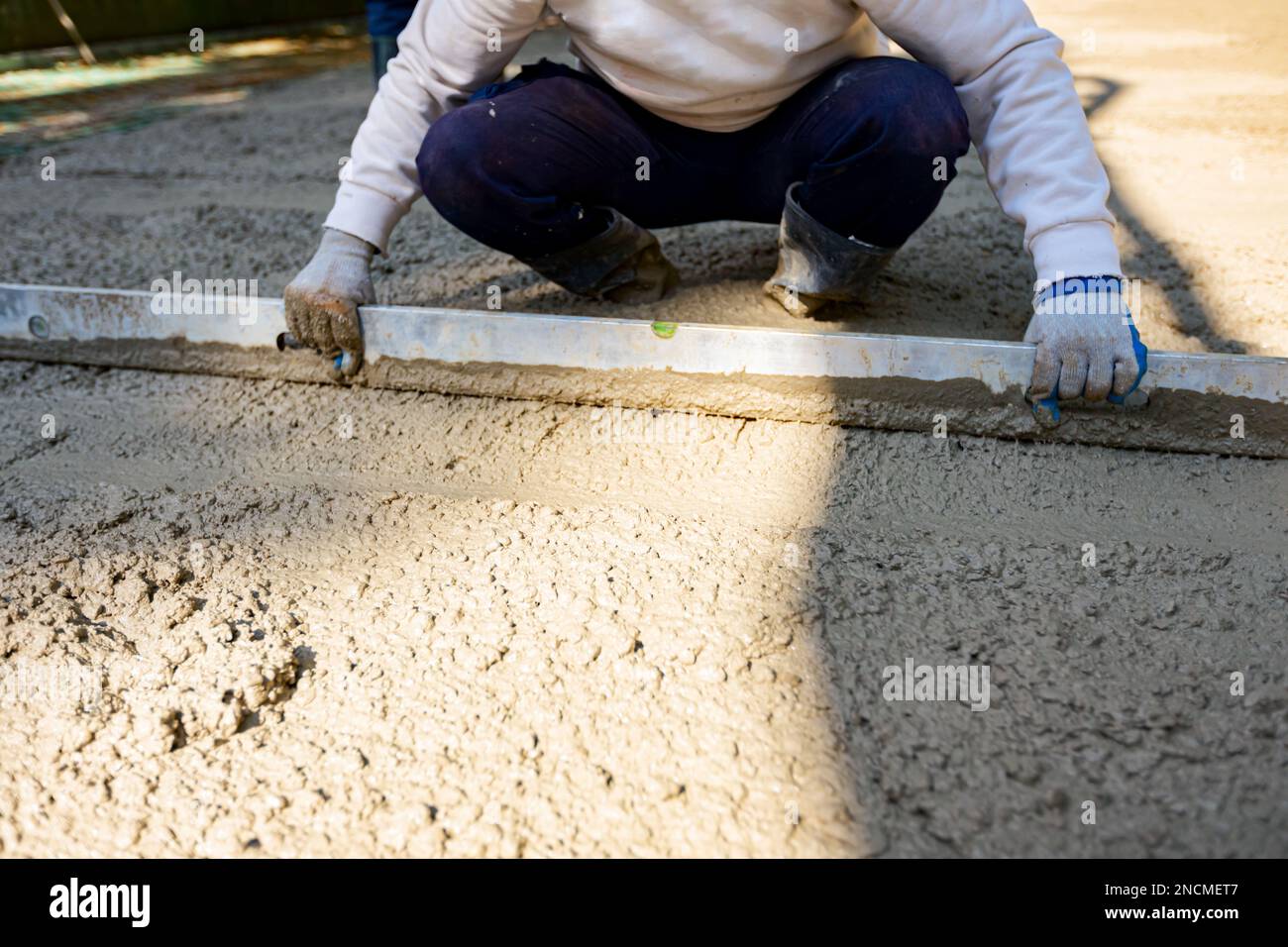 Le travailleur de la construction porte des gants pour niveler le béton frais avec la latte
