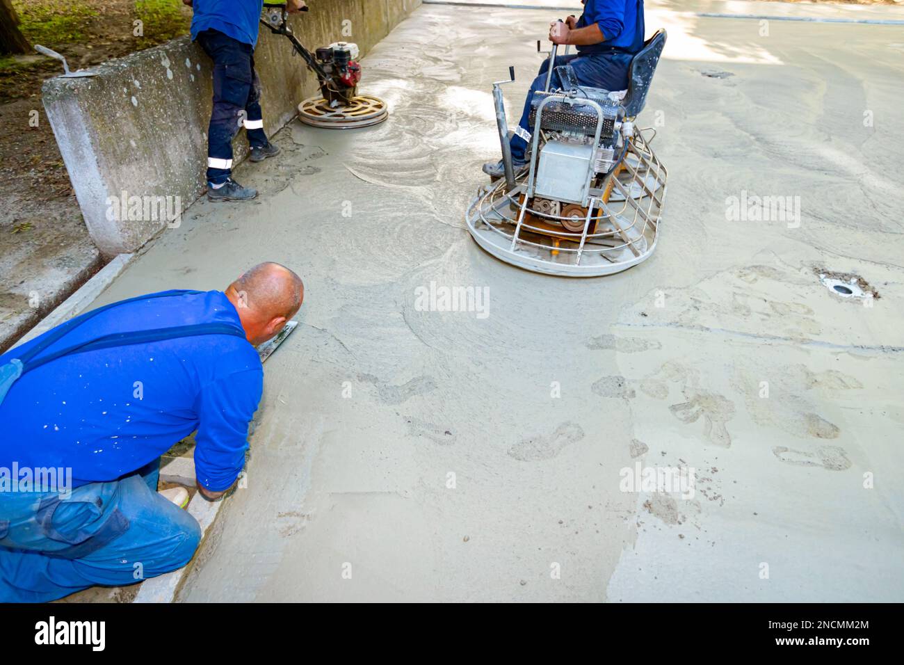 Le travail manuel et le travailleur assis sur une truelle électrique auto-nivelante avec moteur à gaz a des roues avec des plaquettes, plaque et il la conduit en cir Banque D'Images