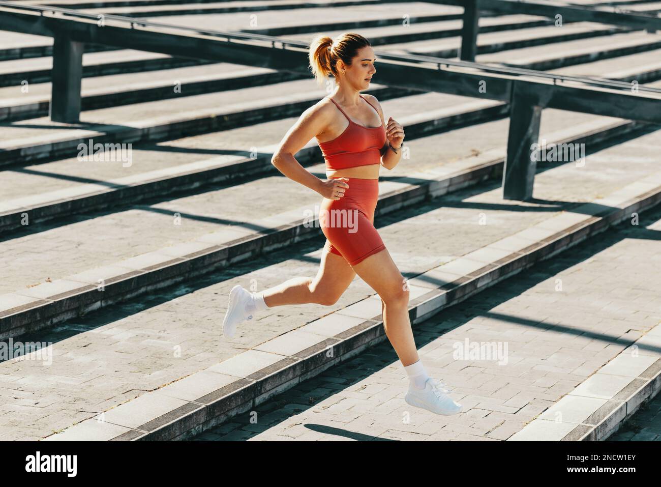 Une femme qui fait du jogging dans les escaliers à l'extérieur le matin. Femme athlétique s'entraîner dans des vêtements de sport. Femme sportive brûlant des calories avec un cardio e Banque D'Images