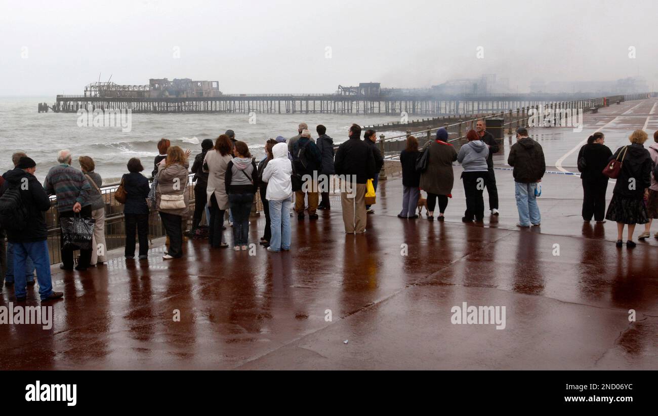People watch the Hastings Pier, after the fire which started in the early hours, in Hastings, England, Tuesday, Oct. 5, 2010. Hastings Pier, a relic of gentler times when mass tourism meant a trip to the seashore, was consumed by fire Tuesday and perhaps marking an end to local hopes to preserve the Victorian relic. Police said they arrested two men, aged 18 and 19, on suspicion of arson. (AP Photo/Sang Tan) Banque D'Images