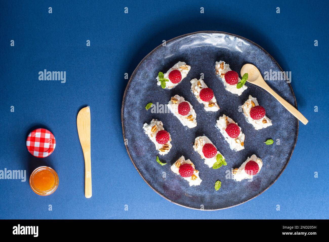 De dessus savoureux dessert appétissant avec crème et framboises servi avec des feuilles de menthe et des noix sur l'assiette près d'un pot de miel avec une cuillère et un couteau Banque D'Images