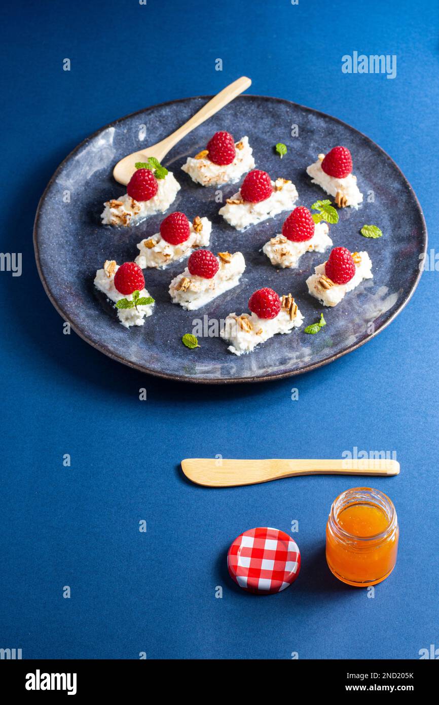 Délicieux dessert appétissant avec crème et framboises servi avec des feuilles de menthe et des noix sur l'assiette près d'un pot de miel avec une cuillère et un couteau Banque D'Images