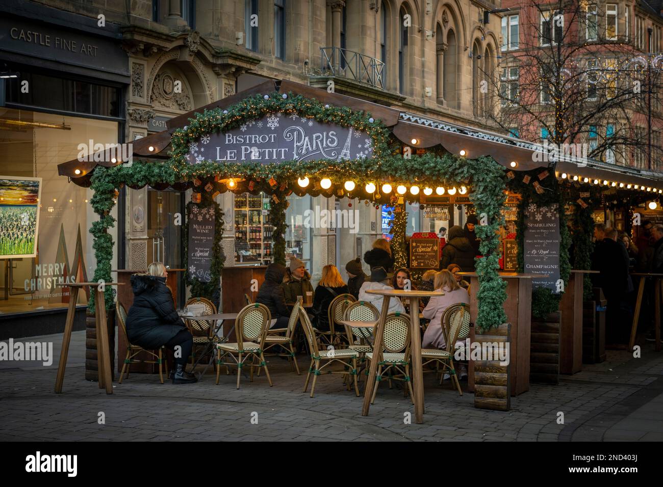 Personnes assises à des tables à l'extérieur du chalet en bois de Bistrot le petit Paris, partie des marchés de Noël de Manchester. ROYAUME-UNI Banque D'Images