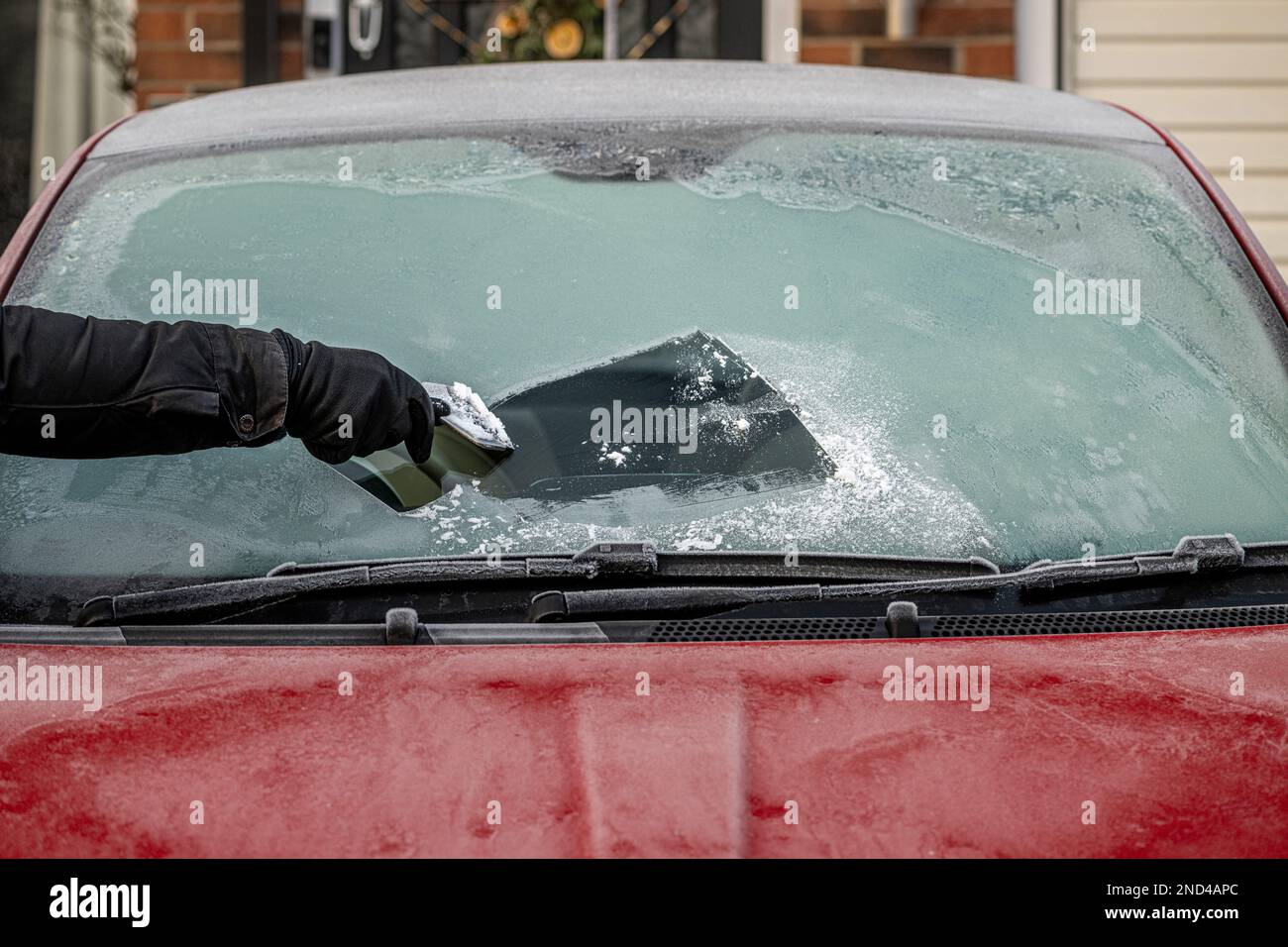 Main gantée tenant un grattoir à glace, éliminant la glace du pare-brise avant d'une voiture gelée. ROYAUME-UNI Banque D'Images