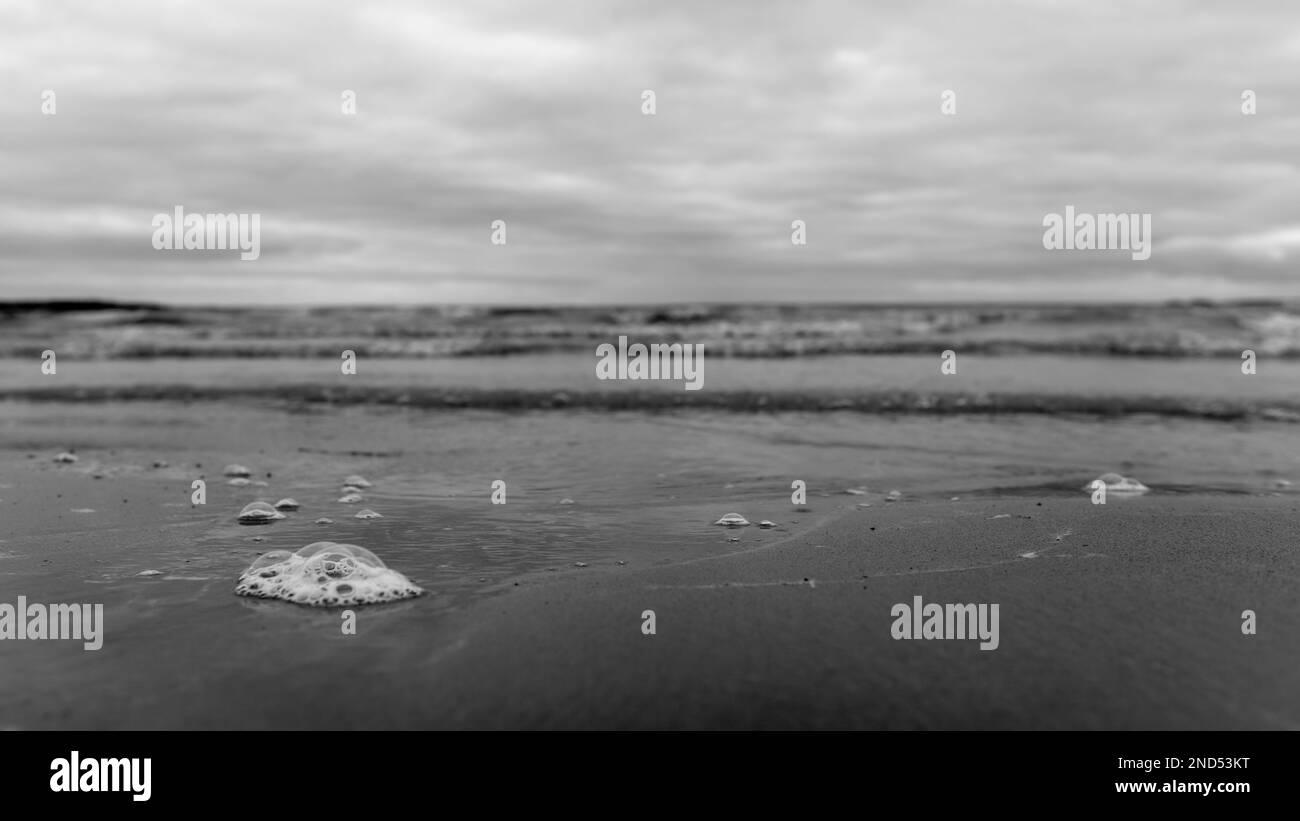 Photo en noir et blanc d'une bulle sur le sable avec un divorce des vagues sur le fond de la mer troublée et du ciel nuageux pluvieux. Banque D'Images