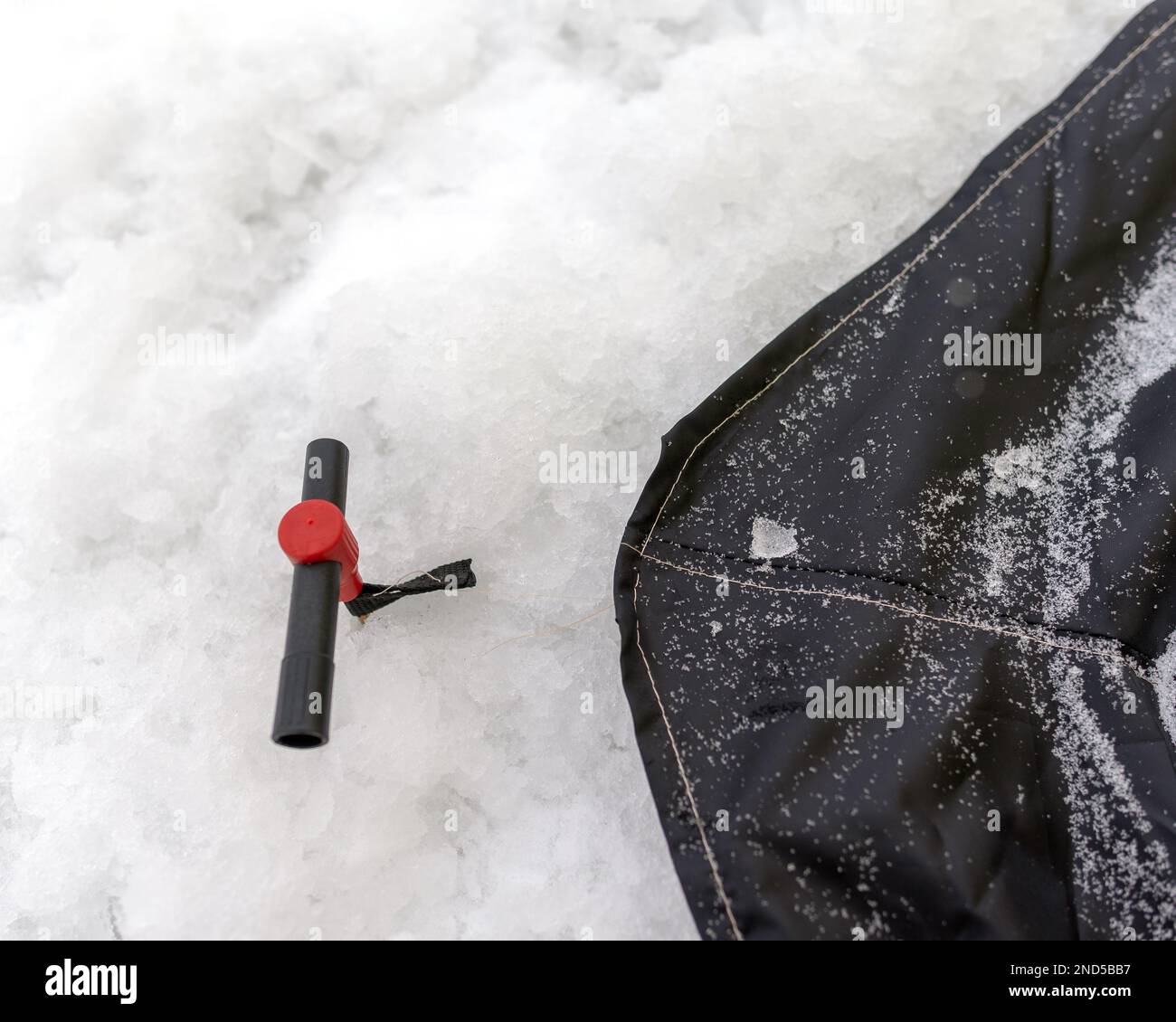 Vis à ergot pour fixer les tentes d'hiver de pêche touristique à la glace est vissé dans la neige avec un support déchiré à la jupe de la tente. Banque D'Images
