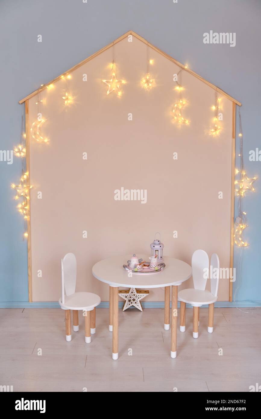 Petite table avec table à thé et chaises avec oreilles de lapin dans la chambre des enfants, lumières à DEL. Blanc et bois. Style Scandi Banque D'Images