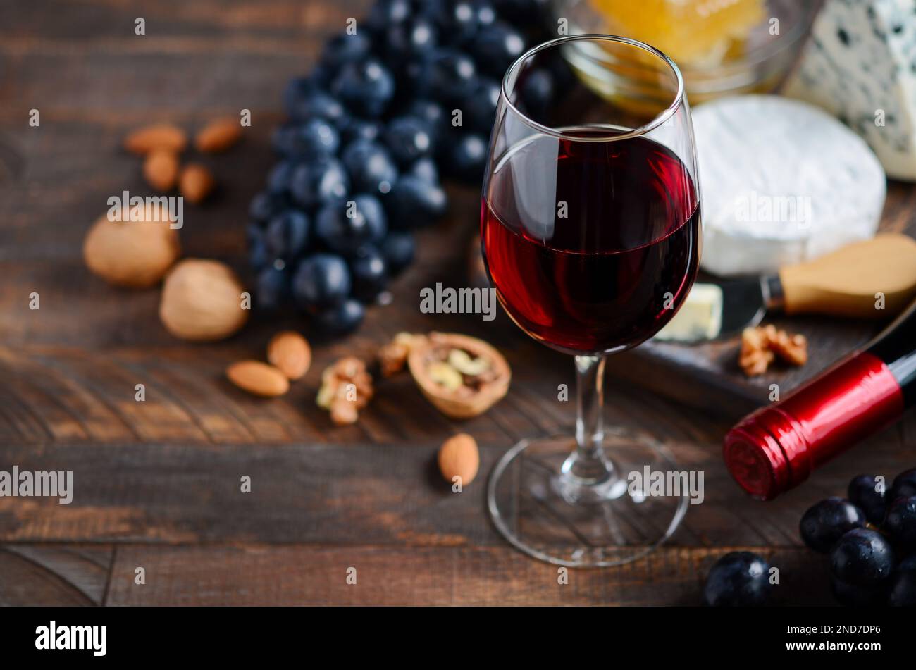 Verre à vin rouge avec fromage, raisins, miel et noix sur une table en bois. Banque D'Images