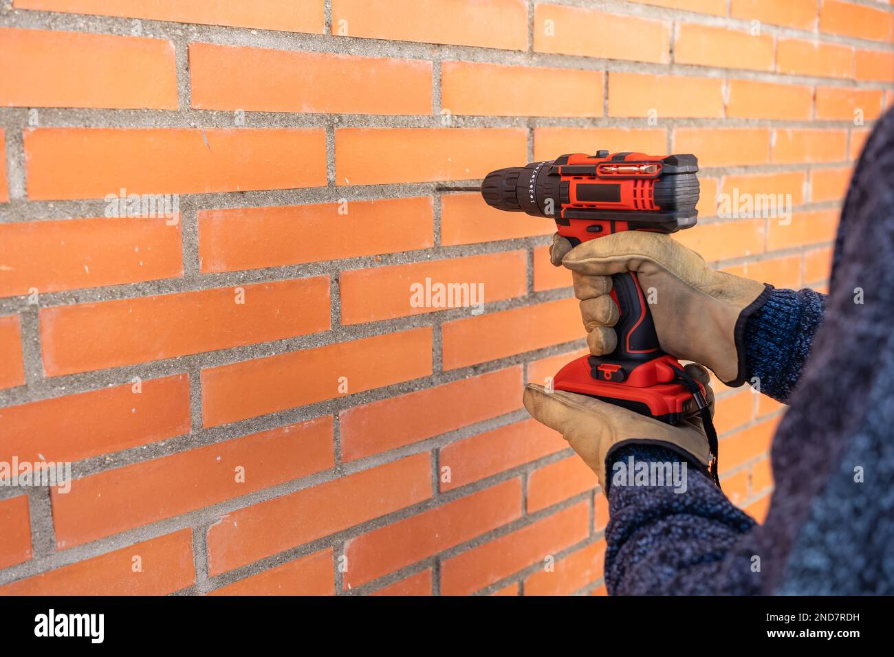 Foreuse avec batterie faisant des trous dans un mur de briques à l'extérieur. Banque D'Images