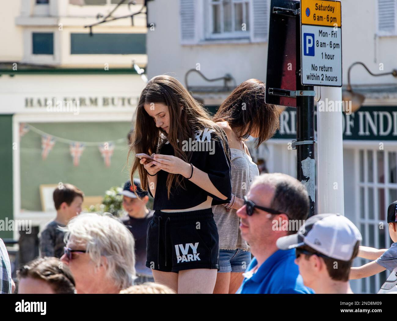 À la manière de beaucoup d'adolescents, une fille qui a grimpé pour regarder la course de soapbox regarde son téléphone Banque D'Images