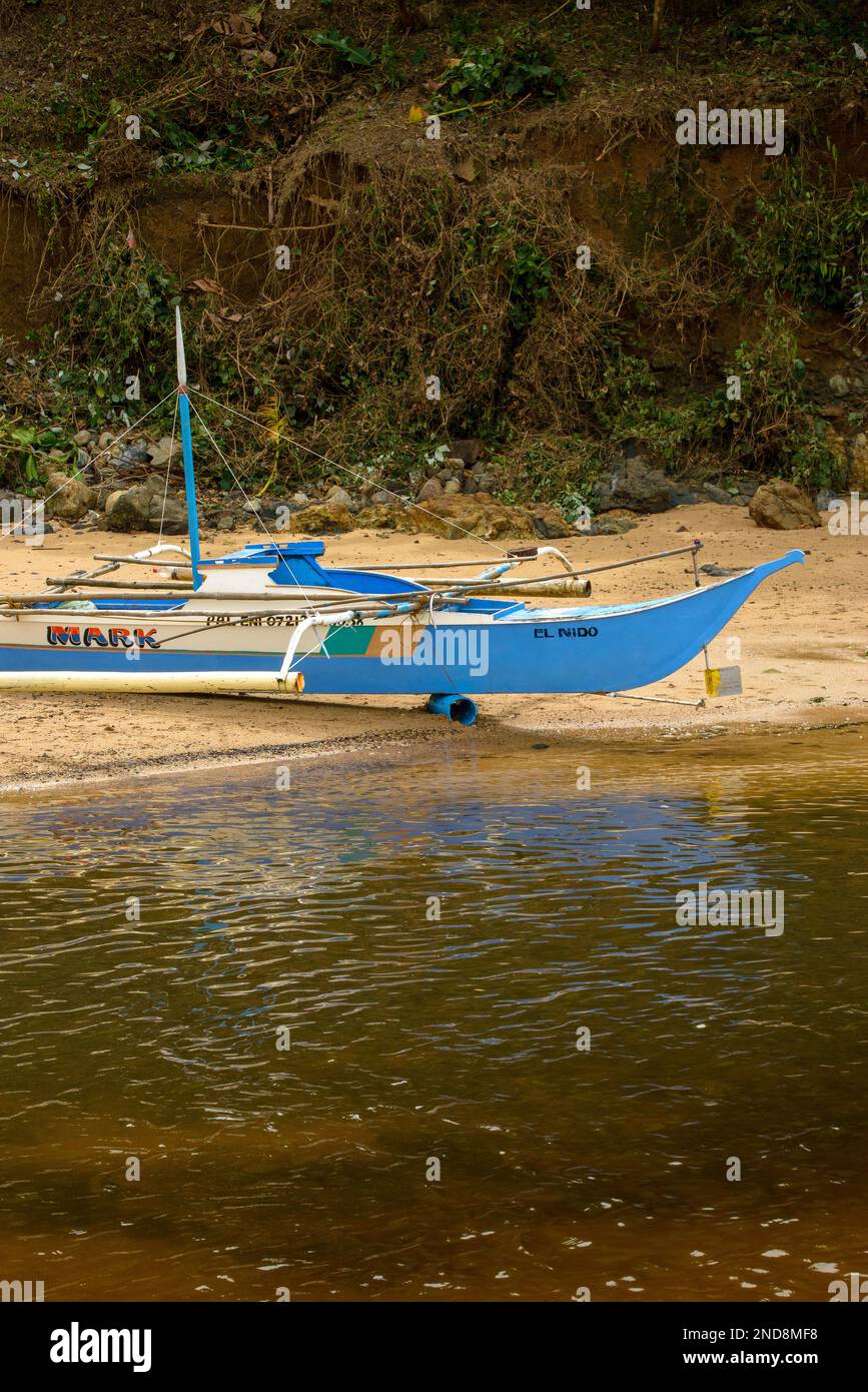 Cette photo capture l'essence des Philippines, avec un bateau traditionnel en bois qui navigue sur des eaux turquoise cristallines, entouré d'un vert luxuriant Banque D'Images