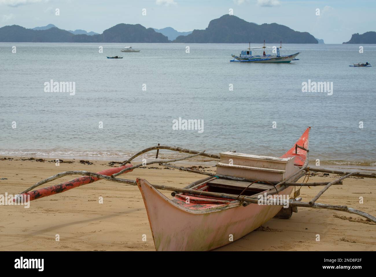 Cette photo capture l'essence des Philippines, avec un bateau traditionnel en bois qui navigue sur des eaux turquoise cristallines, entouré d'un vert luxuriant Banque D'Images