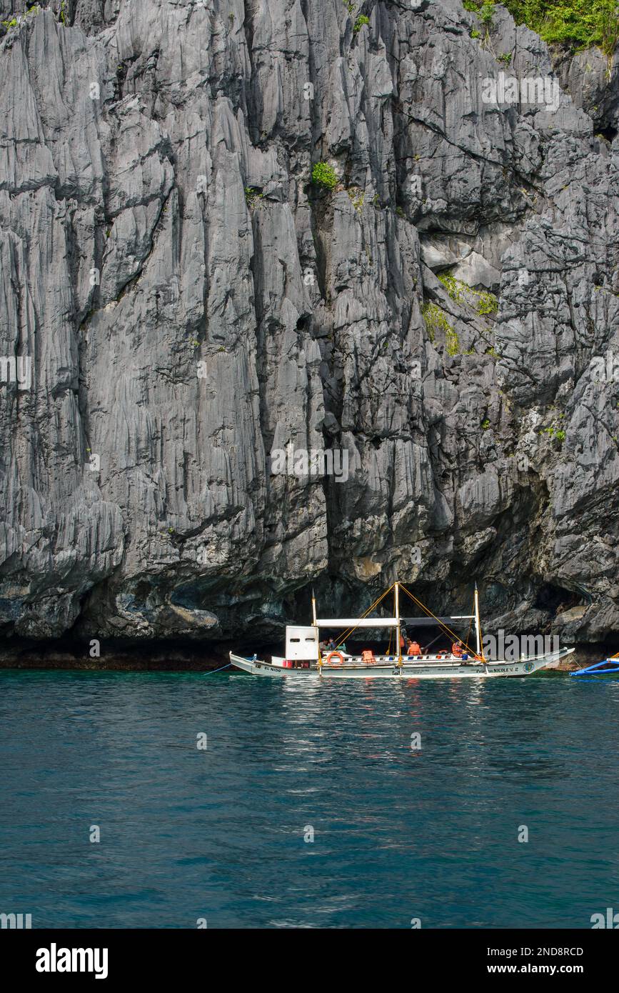 Cette photo capture l'essence des Philippines, avec un bateau traditionnel en bois qui navigue sur des eaux turquoise cristallines, entouré d'un vert luxuriant Banque D'Images