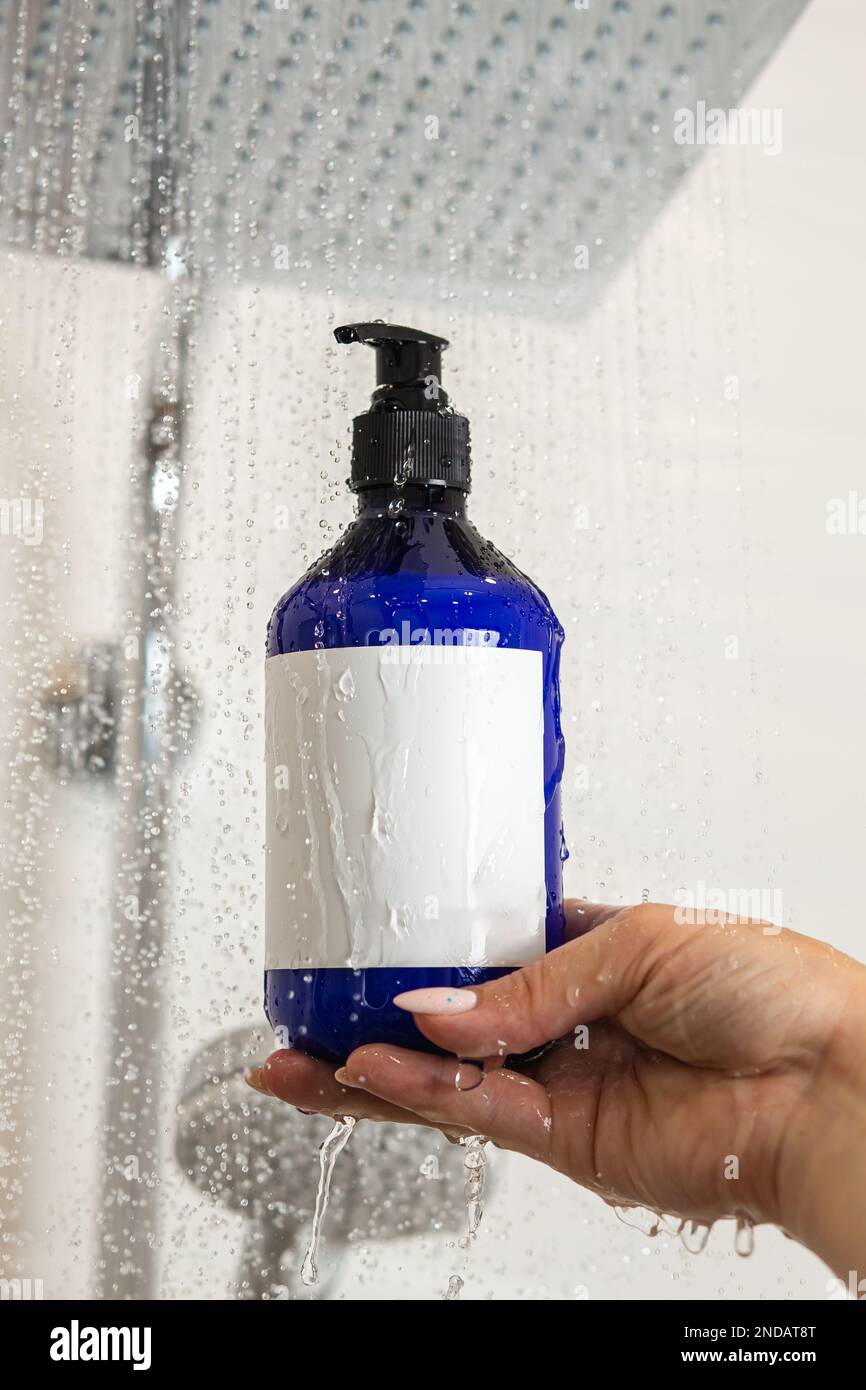 Bouteille couverte de gouttes d'eau dans la main femelle sur la douche. Concept de cosmétiques pour les soins de la peau. Banque D'Images