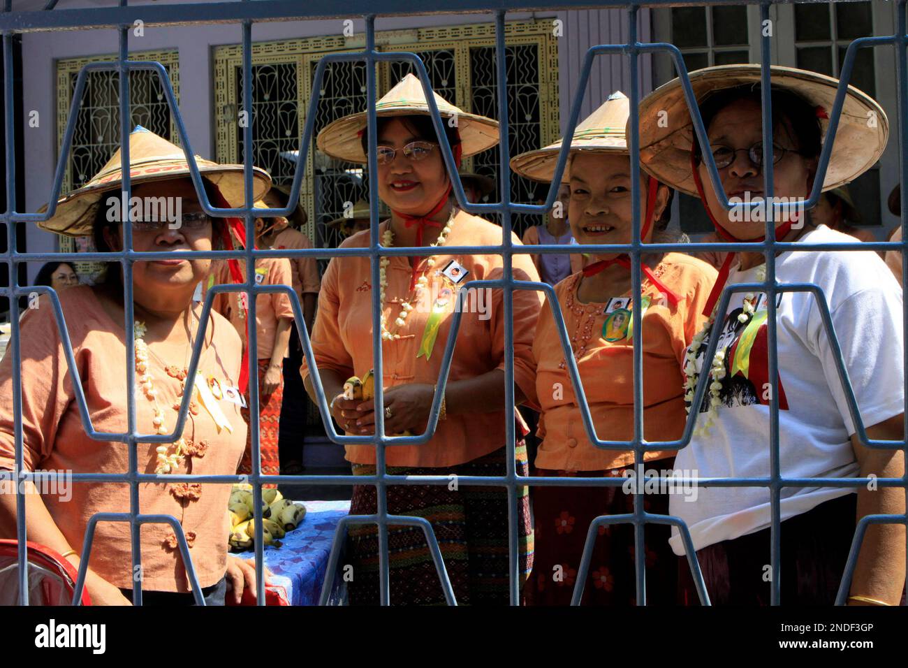 In this photo taken March. 29, 2010, wearing bamboo hat, members of the detained pro-democracy leader Aung San Suu Kyi's National League for Democracy Party stand beyond a gate at the party's headquarters in Yangon, Myanmar. Members of detained opposition leader Aung San Suu Kyi's disbanded political party will lodge a complaint against the use of their bamboo hat party symbol by a renegade group, a party official said Monday.The conical bamboo hat commonly used by farmers, or "khamauk" , is the symbol of the National League for Democracy and should not be used by the renegade National Democra Banque D'Images