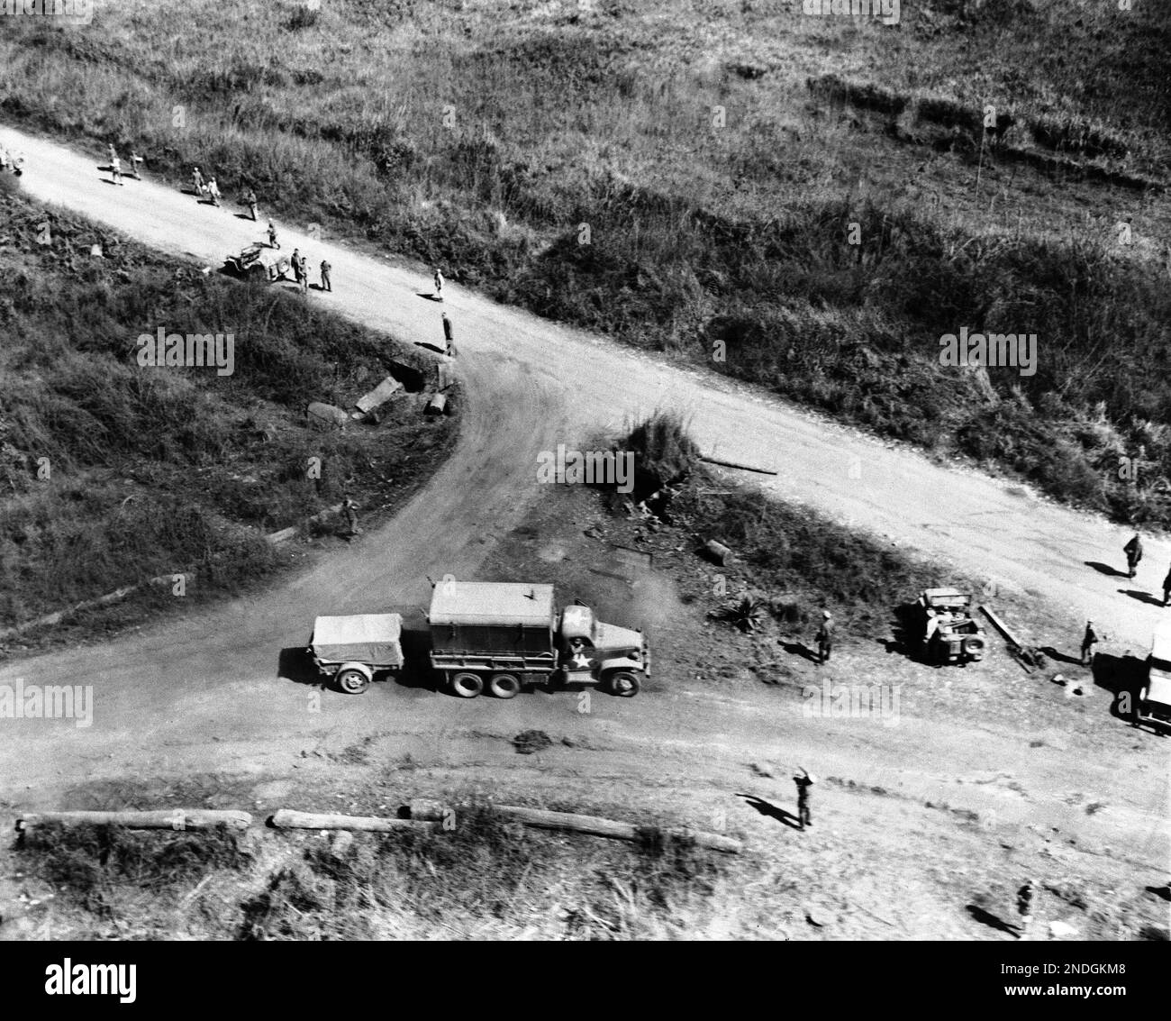 Crossroads of the war in Asia is this junction of the new “Stilwell” Ledo-Burma Road, and the old “Burma Road”, a few miles short of the Chinese border in northern Burma in February 1944. The Stilwell road coming in from India is at the lower left. War supplies make a left turn to continue on to China via the road running out of the photo at upper left. The old Burma Road from Rangoon and lower Burma comes in from the right. The truck and trailer are being waved on to take the turn to China instead of mistakenly keeping straight ahead—and running into Japanese held territory further south. (AP Banque D'Images