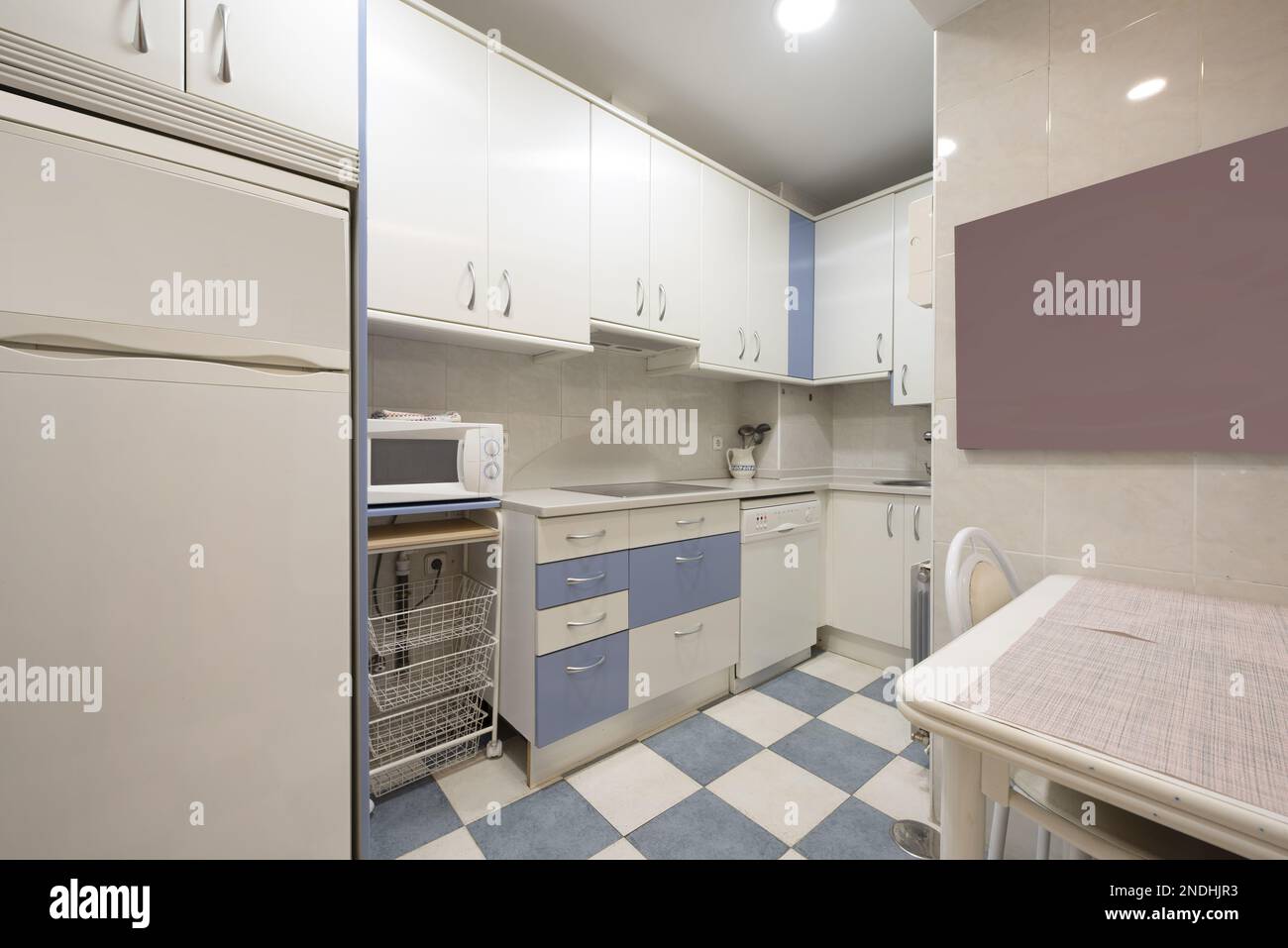 Cuisine avec armoires en bois blanc avec touches bleues, carreaux de couleur assortie, comptoirs en pierre blanche et appareils électroménagers blancs encastrés Banque D'Images