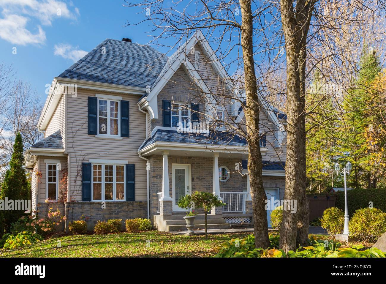 Façade de maison de style cottage en brique et vinyle brun clair avec garniture bleue et toit en bardeaux d'asphalte en automne. Banque D'Images