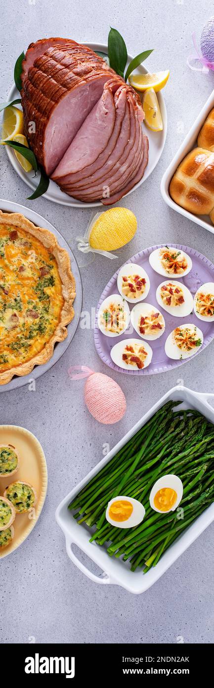 Table de brunch de Pâques avec jambon, quiche, petits pains à croix chaude et œufs dévorés, bannière verticale Banque D'Images