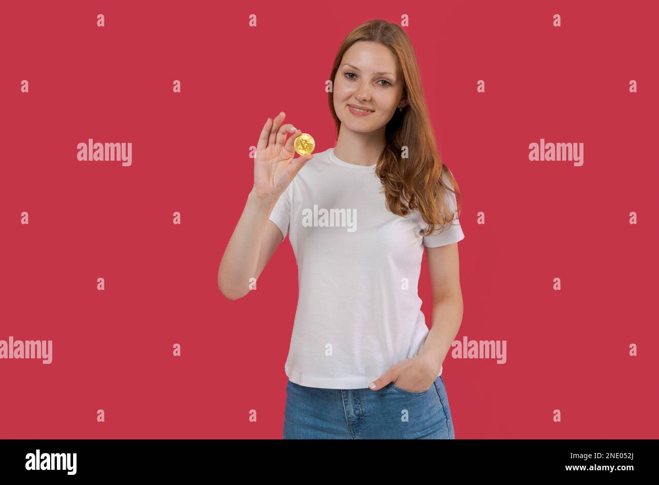 Jeune femme d'affaires souriante dans une chemise blanche tenant le bitcoin à la main posant isolée sur fond de mur rose. Concept d'entreprise de patrimoine de carrière. Placez-le sur une copie de l'emplacement. Banque D'Images