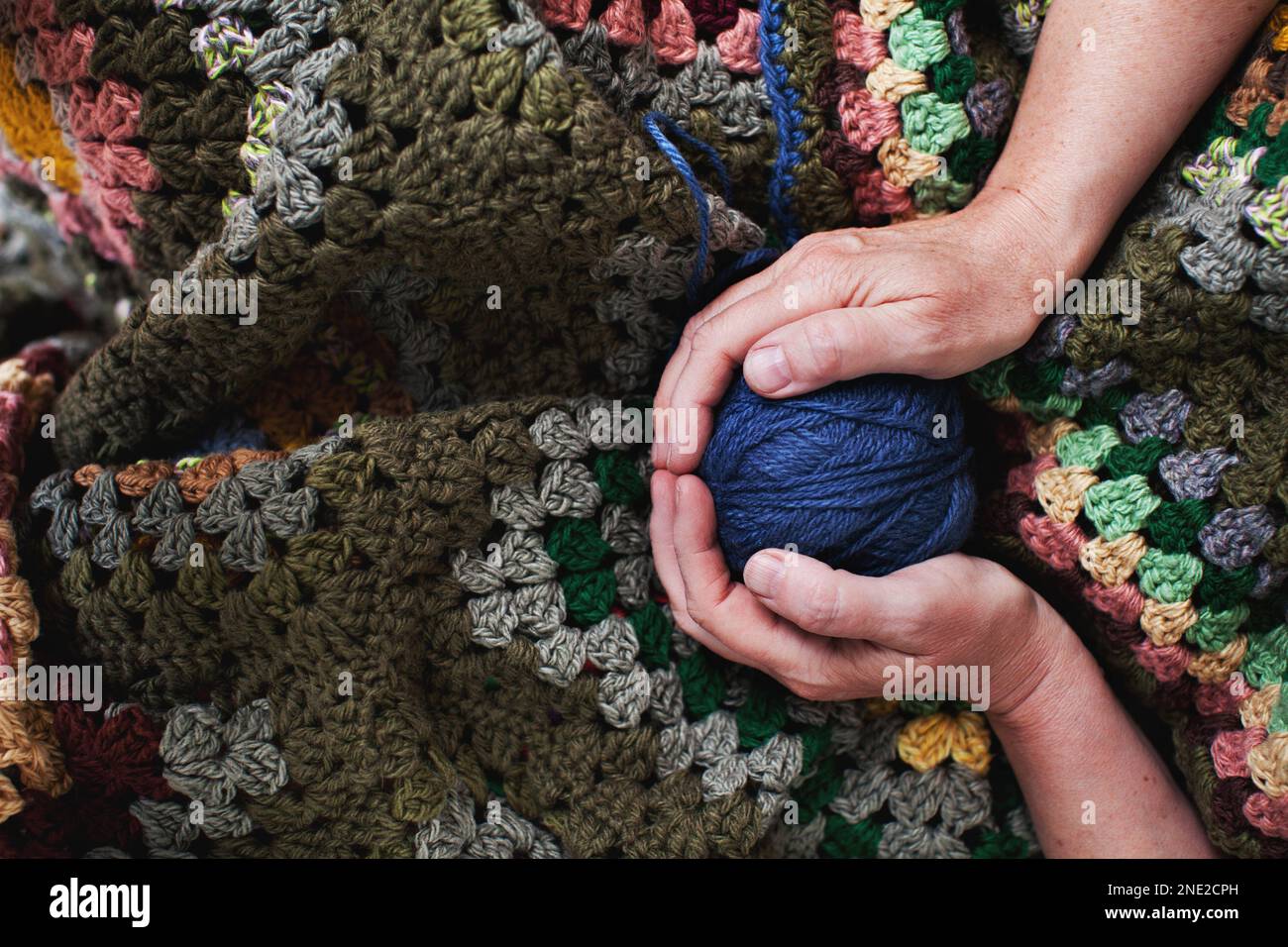 Femme âgée avec une boule de fils tricotés en mains sur fond de tissu tricoté Banque D'Images