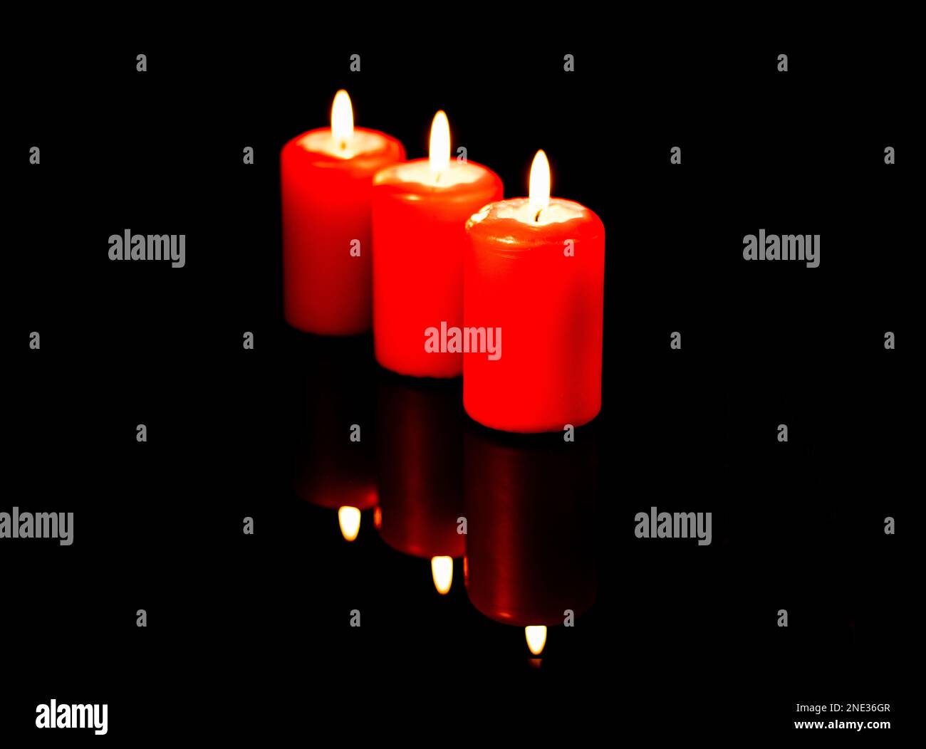 Trois bougies rouges chaudes sont reflétées sur l'arrière-plan d'un miroir noir. Banque D'Images