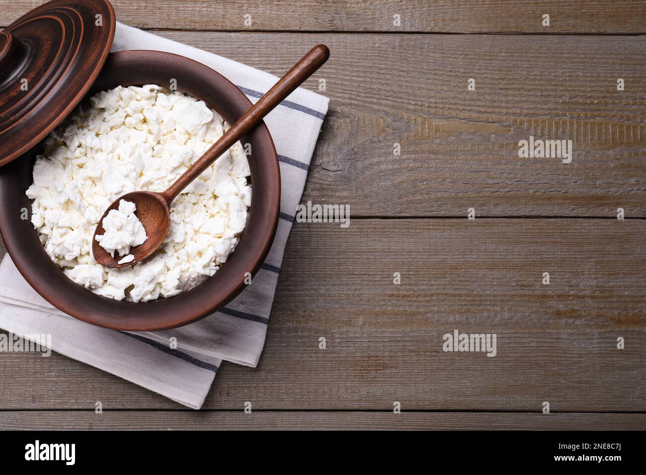 Vue de dessus de pot en argile avec fromage cottage et cuillère sur table en bois gris, espace pour le texte Banque D'Images