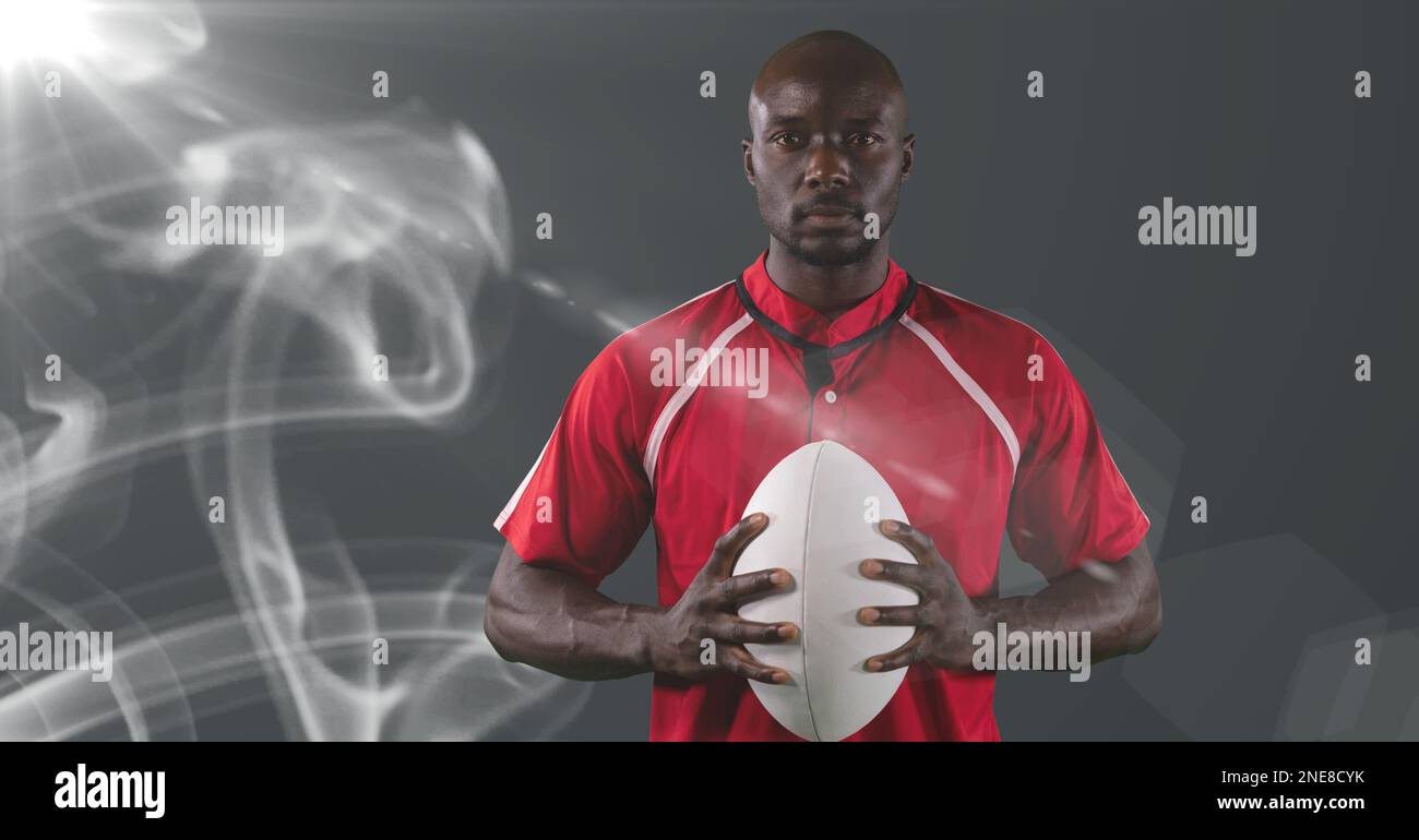 Joueur de rugby afro-américain tenant le ballon contre la fumée et la tache lumineuse sur fond gris Banque D'Images