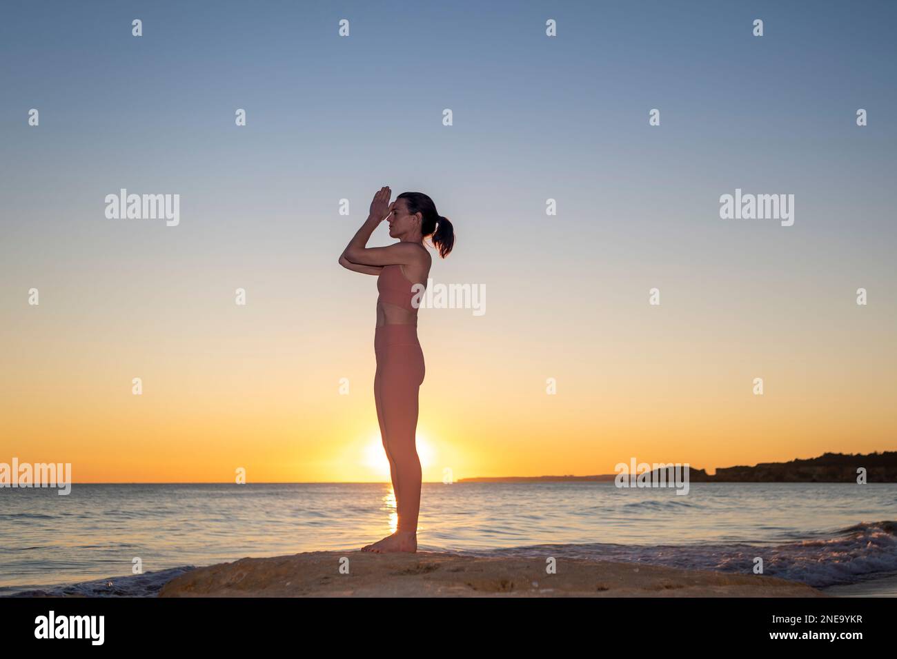 Femme debout près de l'océan au lever du soleil méditant et pratiquant le yoga. Banque D'Images