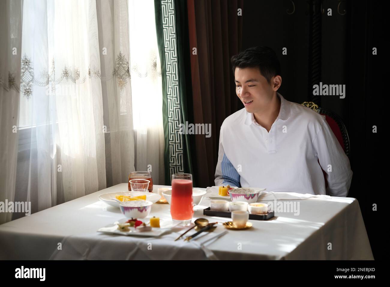 Souriez un jeune homme asiatique charmant assis à côté d'une table de repas fine au restaurant Banque D'Images