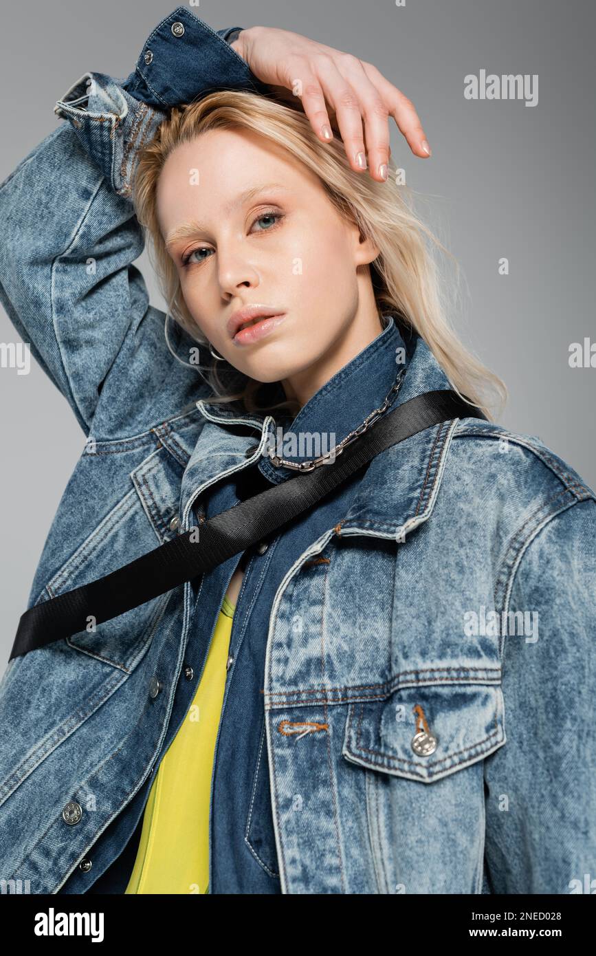 jeune modèle blond avec les yeux bleus regardant la caméra tout en posant isolé sur gris, image de stock Banque D'Images