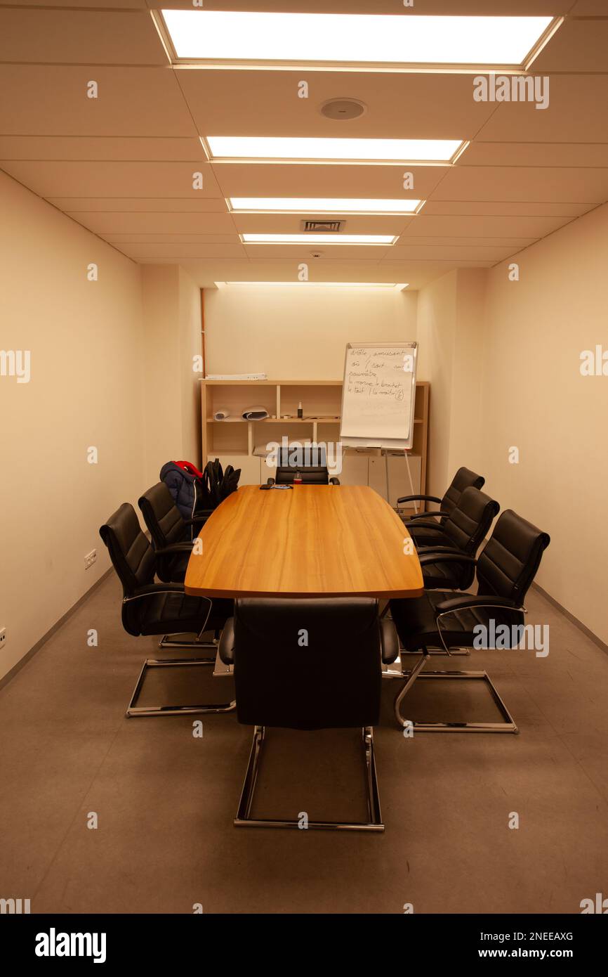 Les chaises noires sont autour d'une table de conférence éclairée par des lumières carrées au plafond. Banque D'Images
