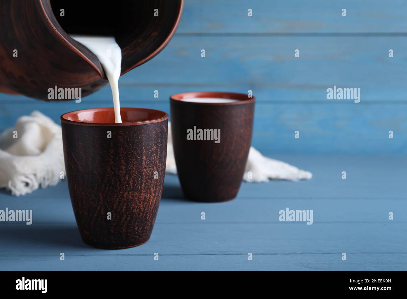 Verser le lait dans une tasse d'argile sur une table en bois bleu clair, espace pour le texte Banque D'Images