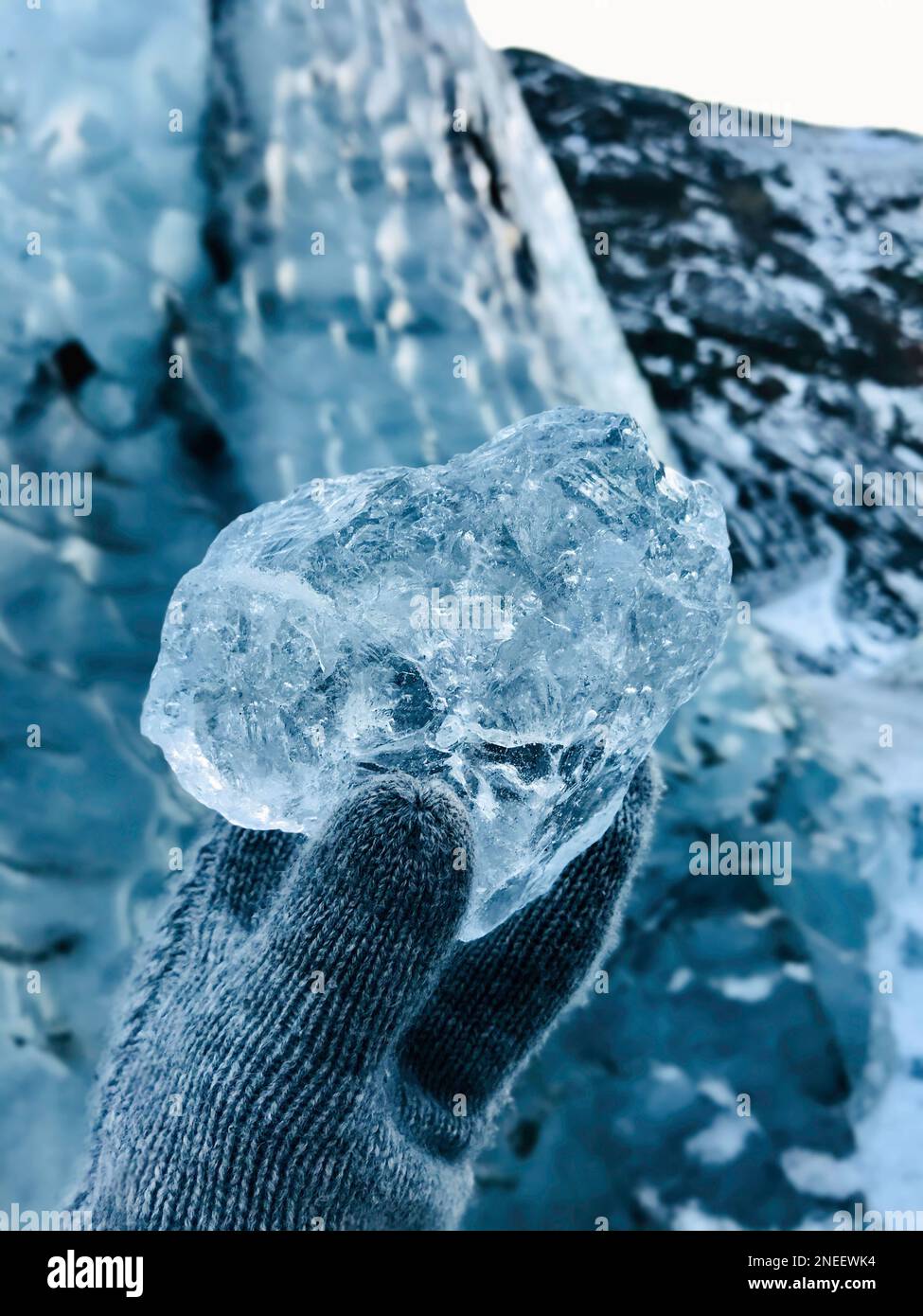 Gros plan de main gantée avec gant tenant un morceau de glace glacé et transparent provenant d'un glacier islandais, scène nordique glacée d'hiver Banque D'Images