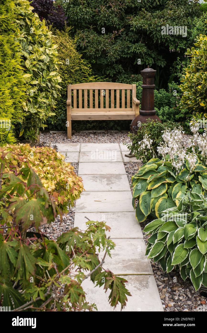 Un banc de jardin en bois et un chimenea dans un jardin verdoyant avec un chemin pavé menant à Banque D'Images