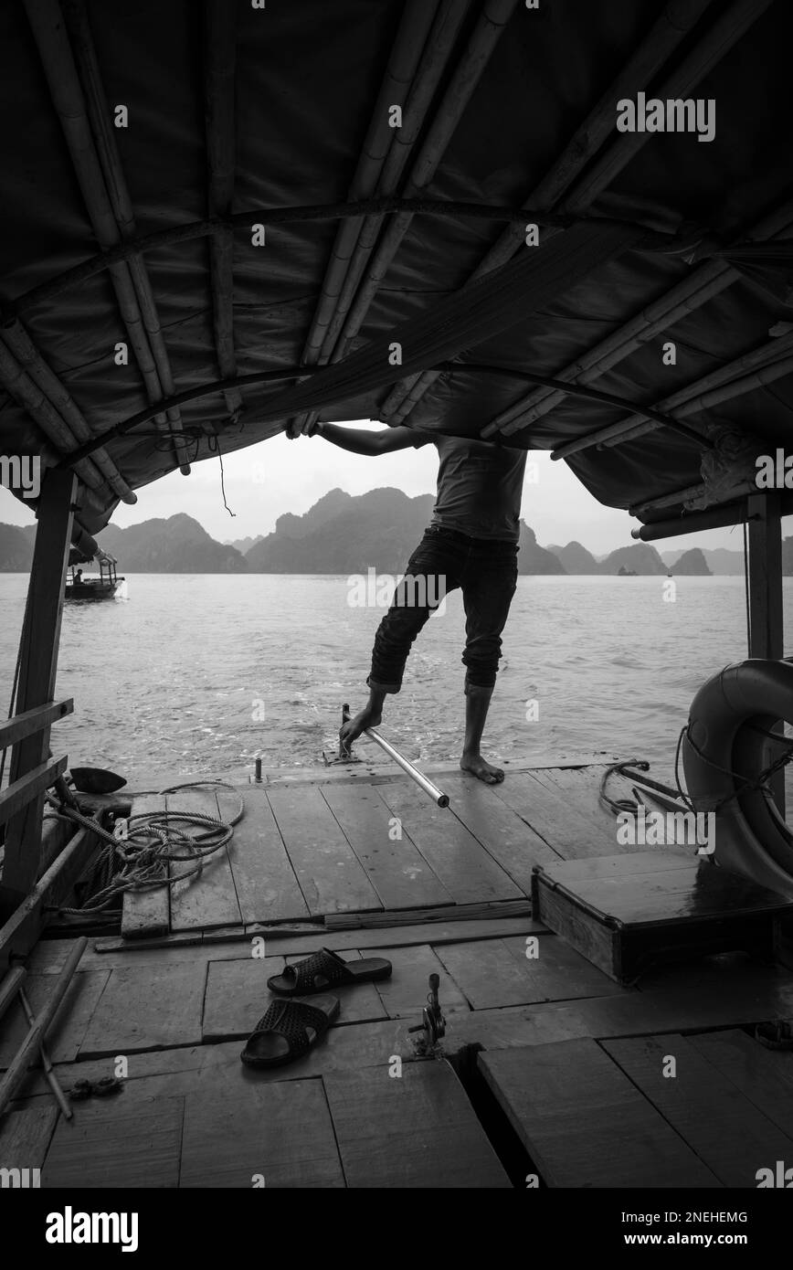 Silhouette noire et blanche d'un homme qui dirige un bateau couvert avec son pied dans la baie d'Ha long. Banque D'Images