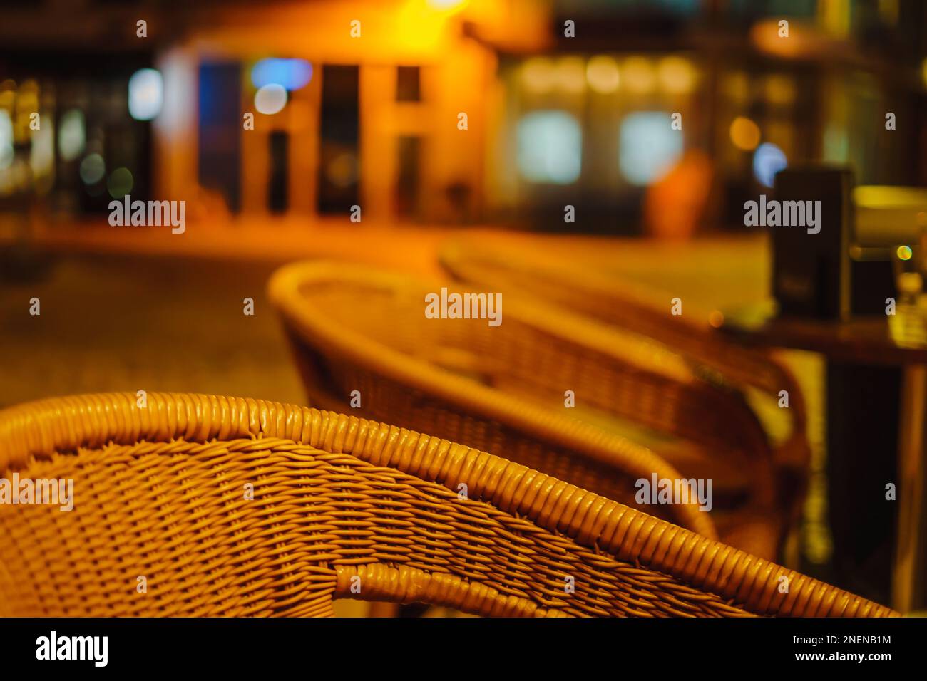 Gros plan des chaises en osier du café restaurant d'été dehors la nuit d'été sans personnes à côté de la lumière jaune de rue Banque D'Images