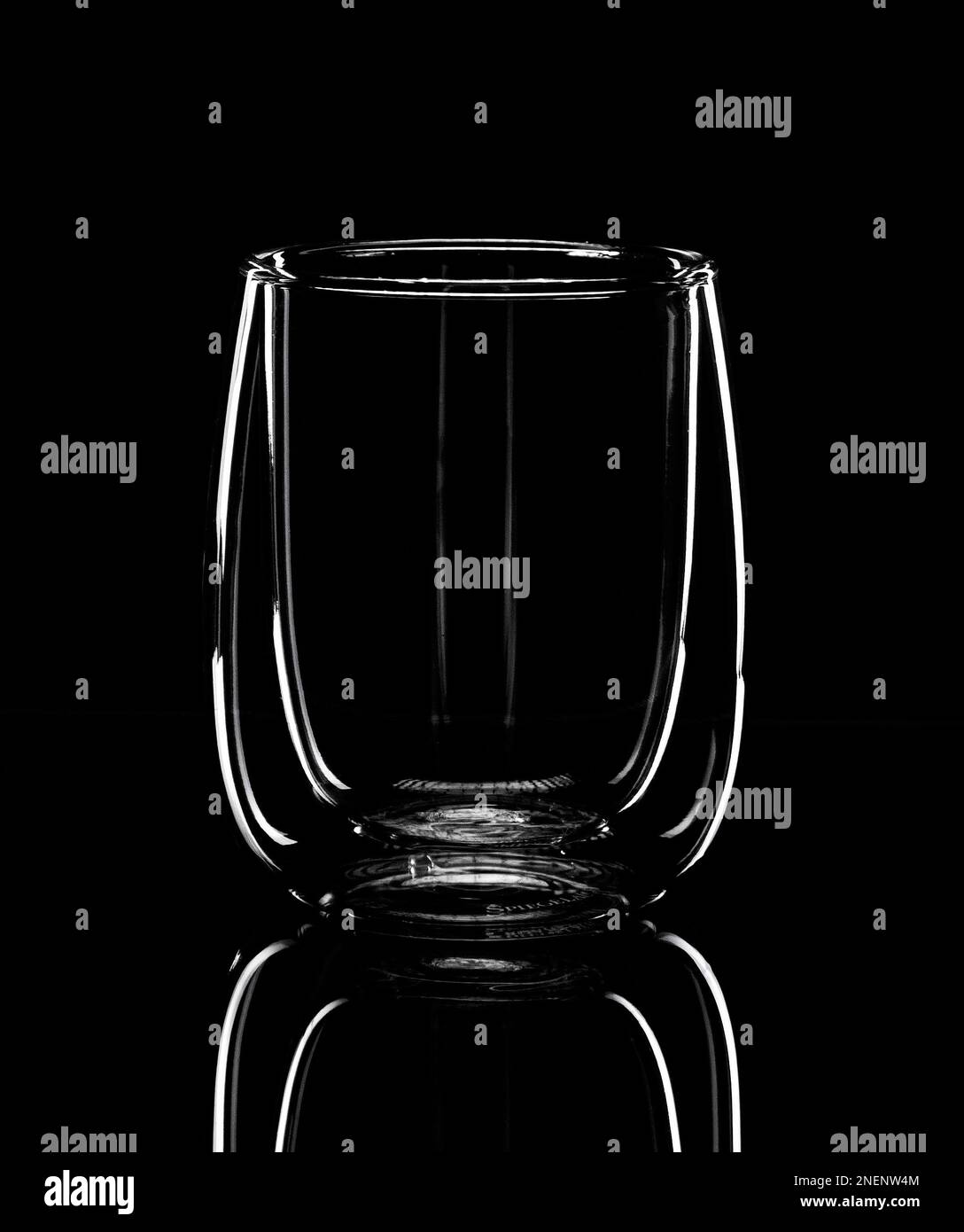 Minimalisme, la silhouette lumineuse d'un verre pour latte se reflète dans une table miroir noire. Photo monochrome Banque D'Images