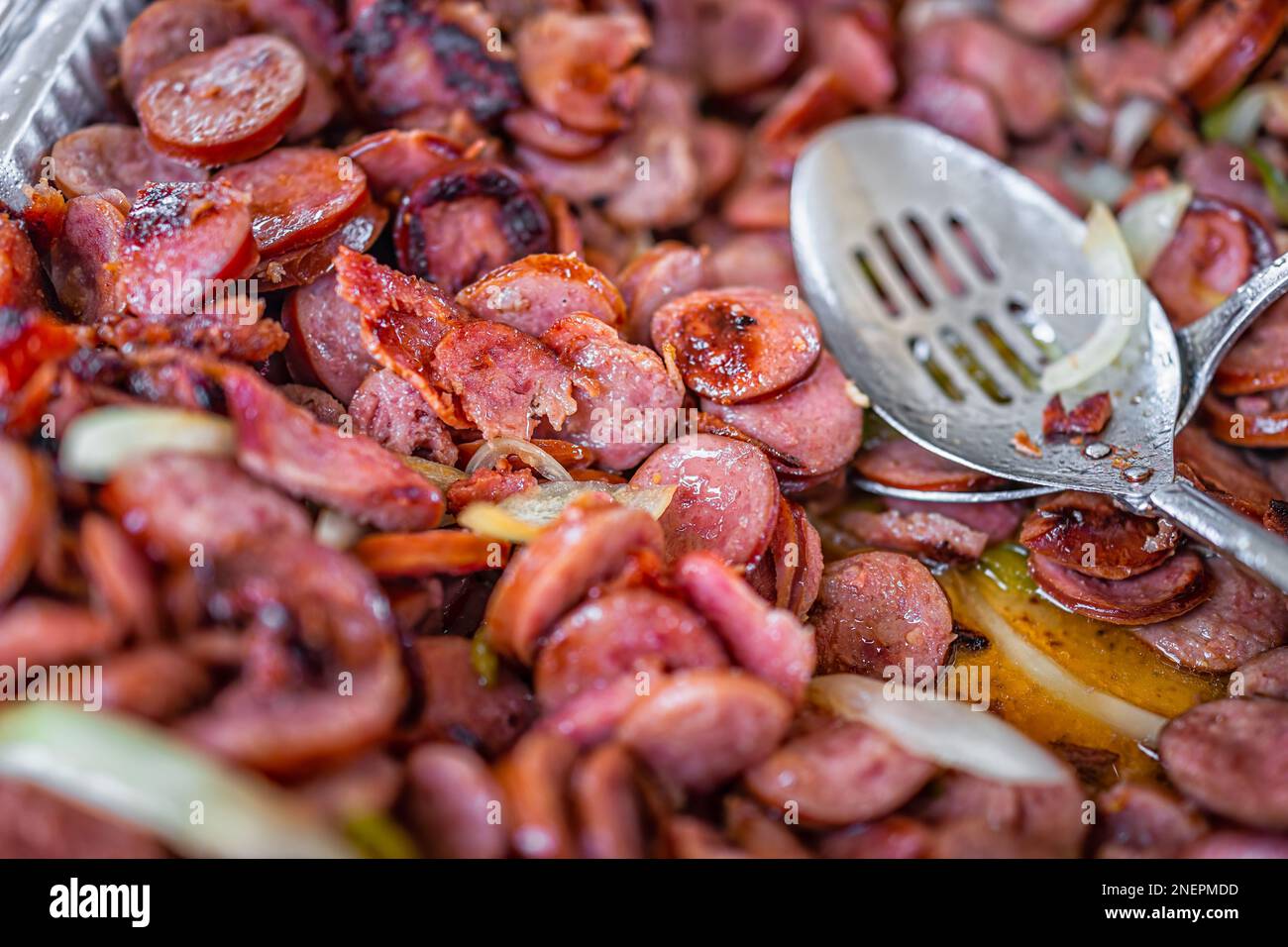 Saucisse de kielbasa calabraise poêlée fumée avec oignon comme plat d'apéritif brésilien Linguica Bebada et cuillère de service dans le plateau de buffet pour la veille Banque D'Images