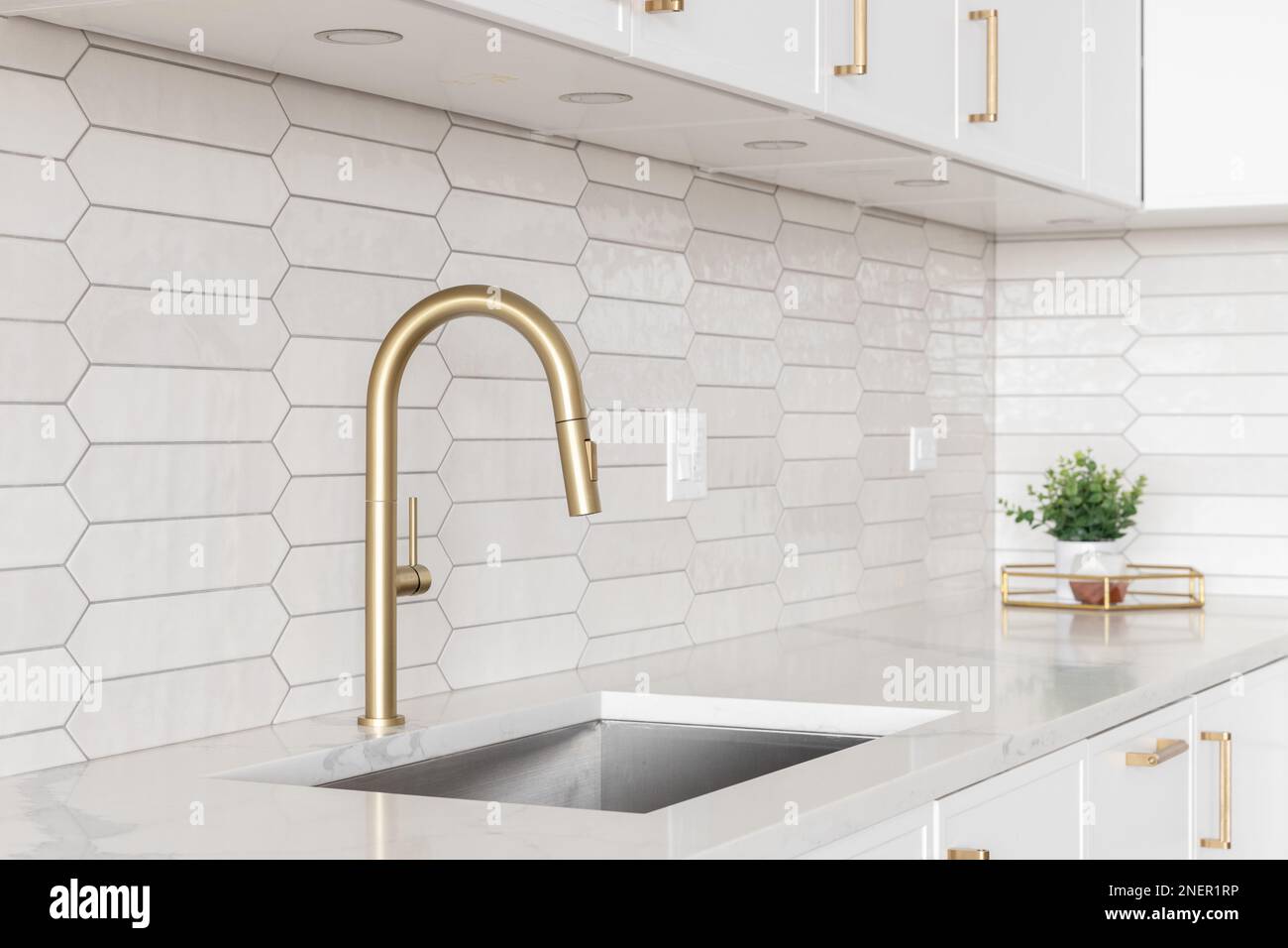 Un beau robinet de cuisine avec des armoires blanches, un robinet d'or, des comptoirs en marbre blanc, et un fond de carreaux de céramique marinés. Banque D'Images