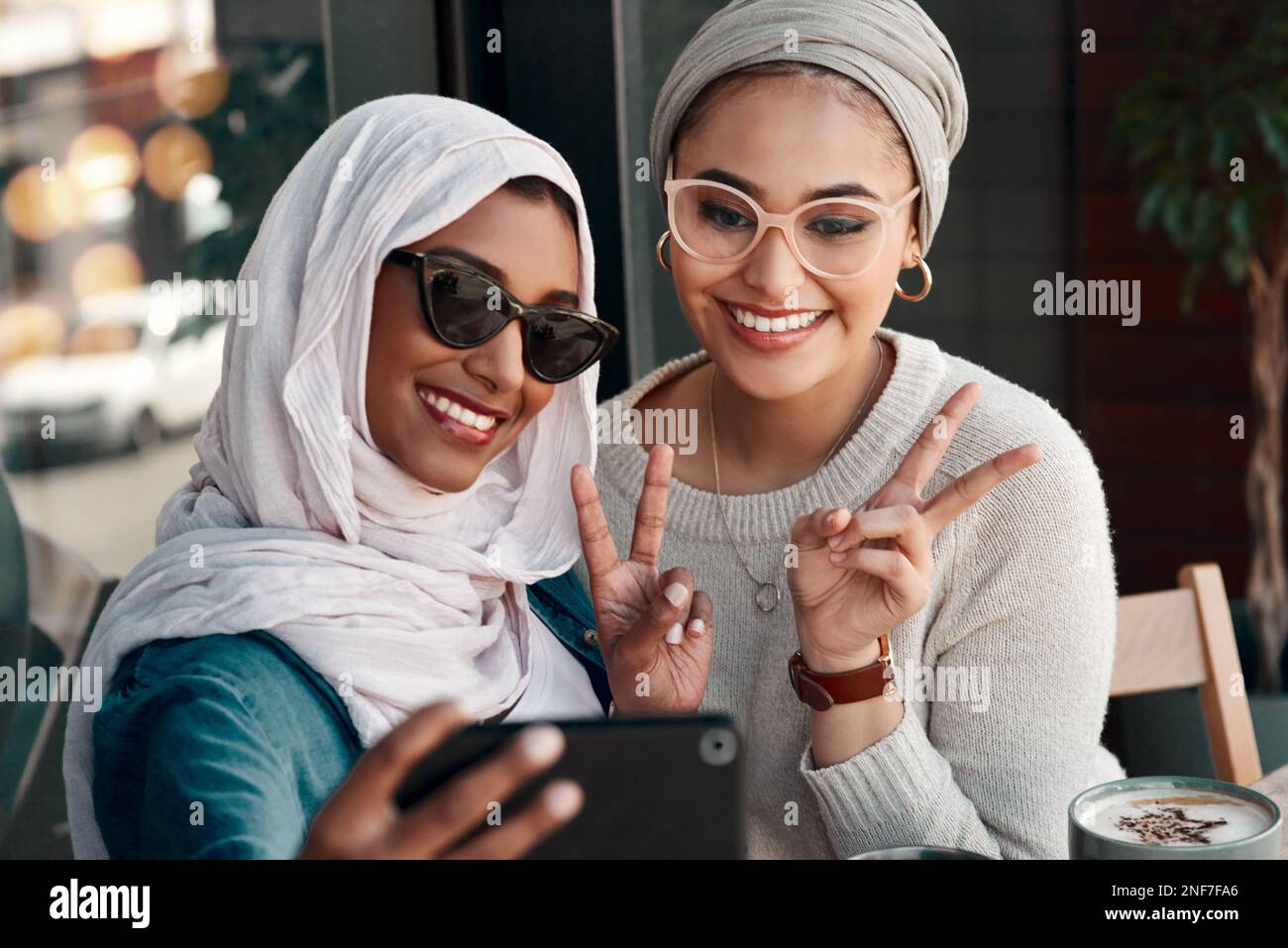 Nous étions ici pour prêcher des gens de la paix. Coupe courte deux jeunes amies affectueuses qui se posent ensemble pour un selfie dans un café tout en étant vêtues de hijab. Banque D'Images